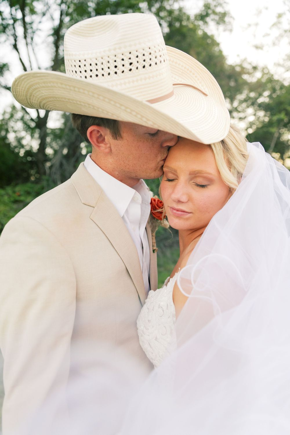 Romantic wedding couple in cowboy hats share intimate moments in a rural outdoor setting.