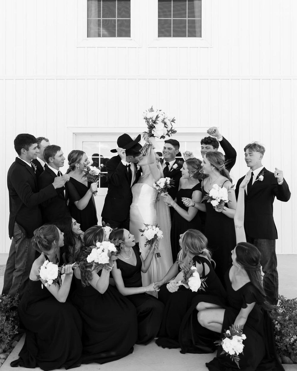 Black and white portrait of wedding party making playful expressions against white wall.