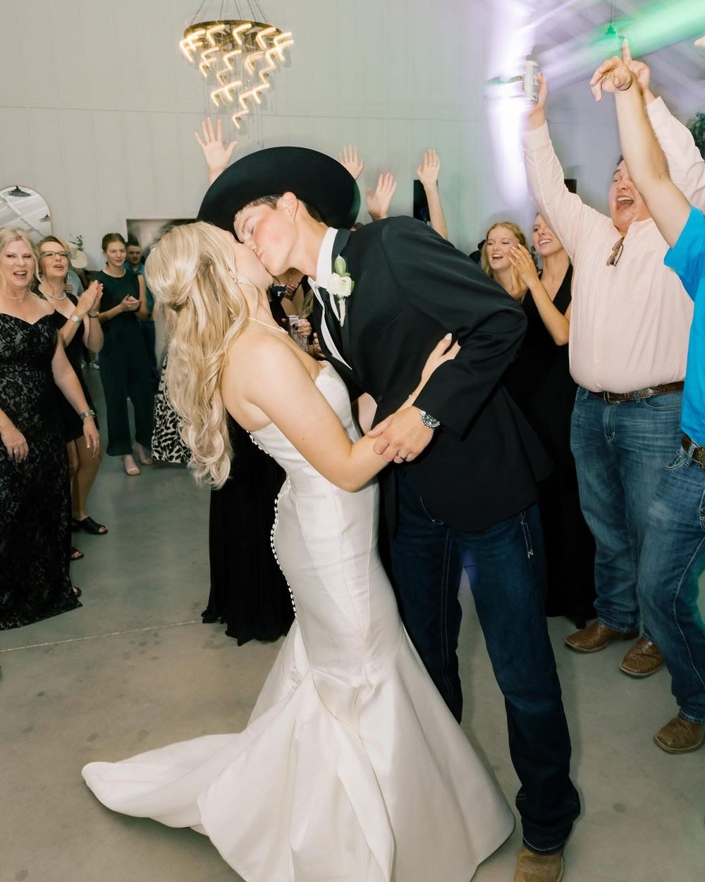 A couple performs a romantic dance dip at their wedding reception while guests cheer in the background.