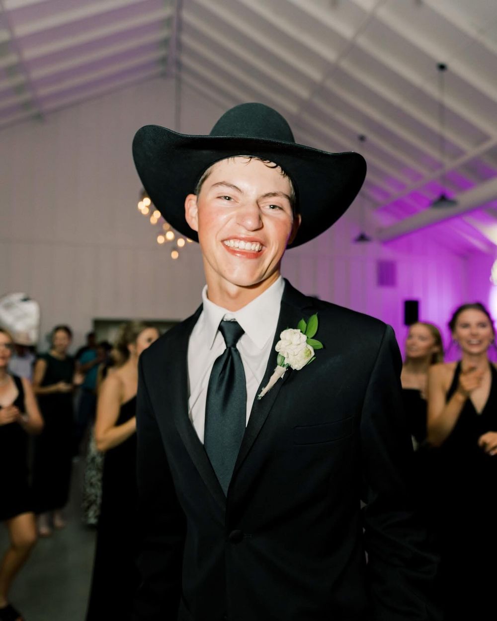 Groom in a black cowboy hat and tuxedo at a wedding reception.