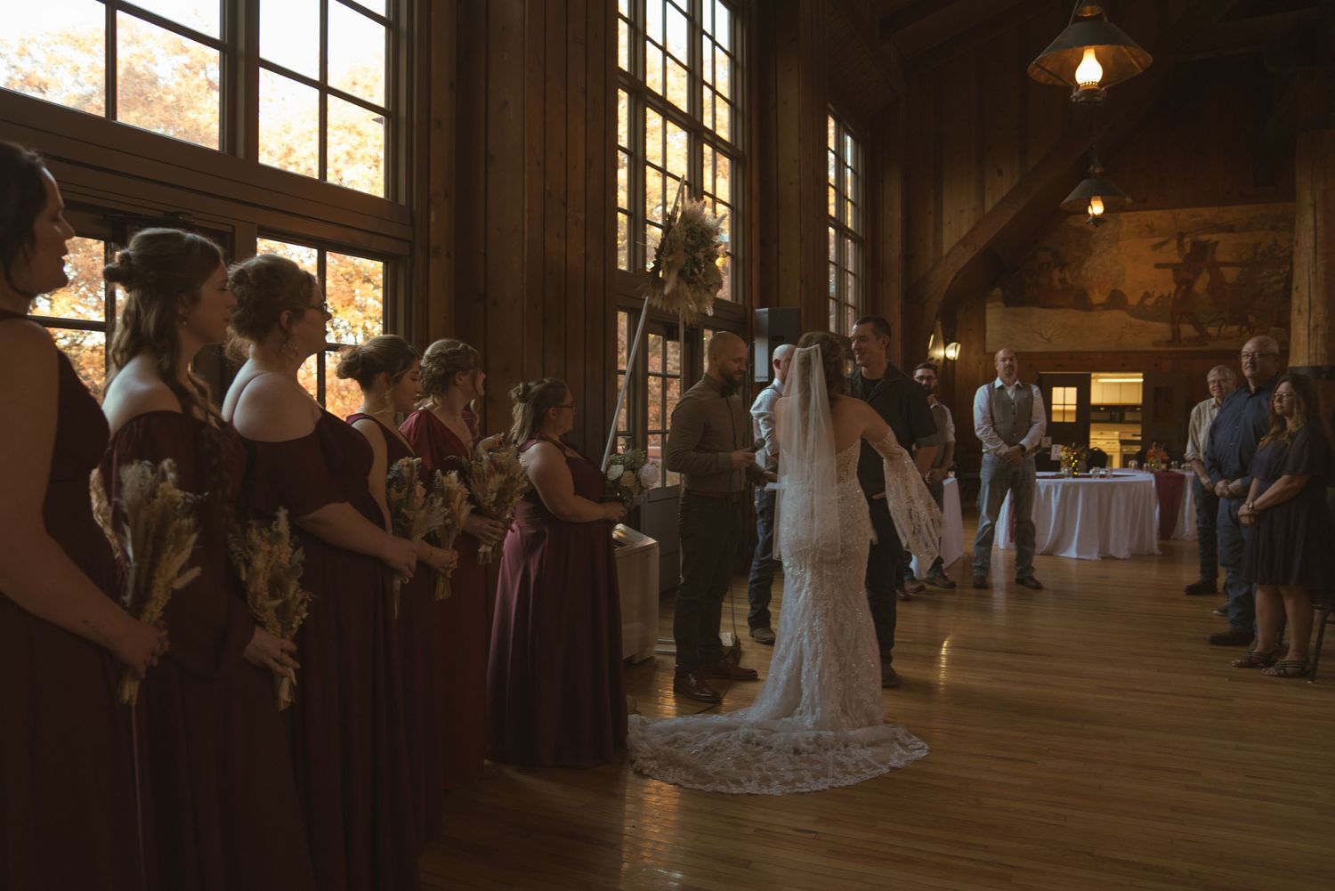 Wedding ceremony in a historic venue with large windows casting natural light across wooden floors.
