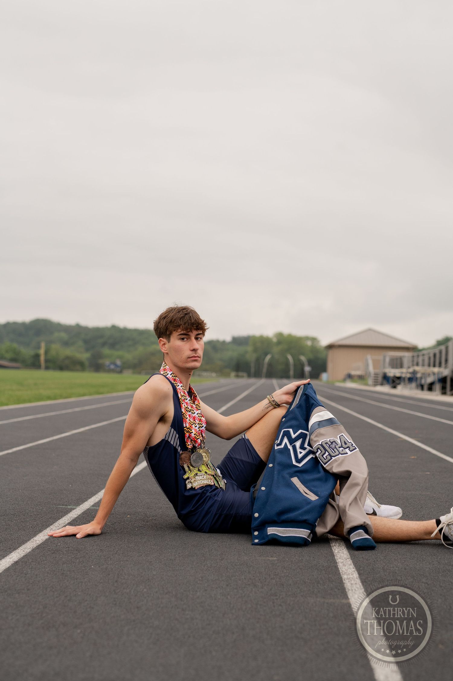 Athlete rests on running track wearing navy uniform and displaying medals.