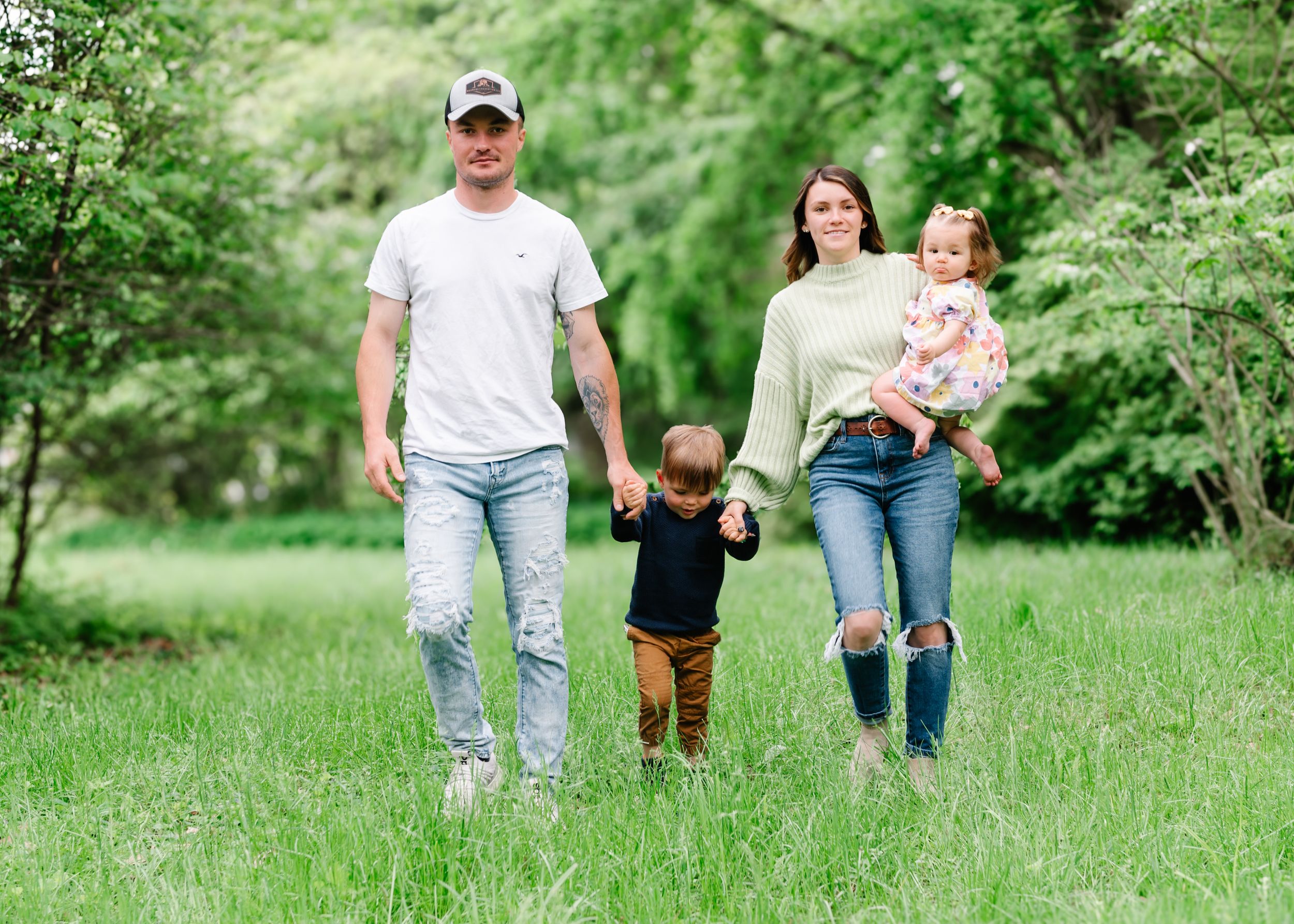 A family walks together through a lush green meadow on a sunny spring day.