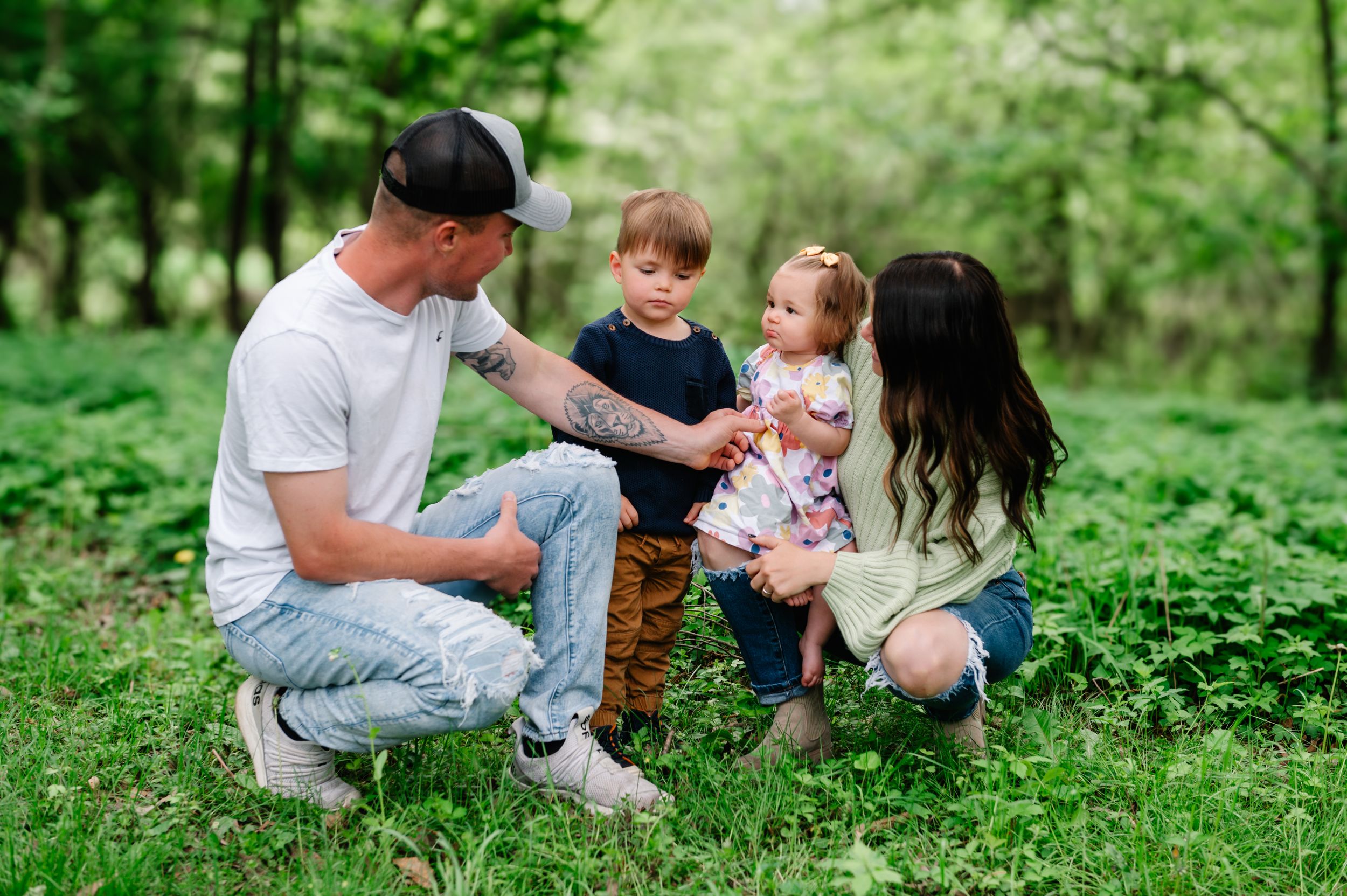 A family enjoys a playful moment together while sitting on green grass in a lush forest setting.