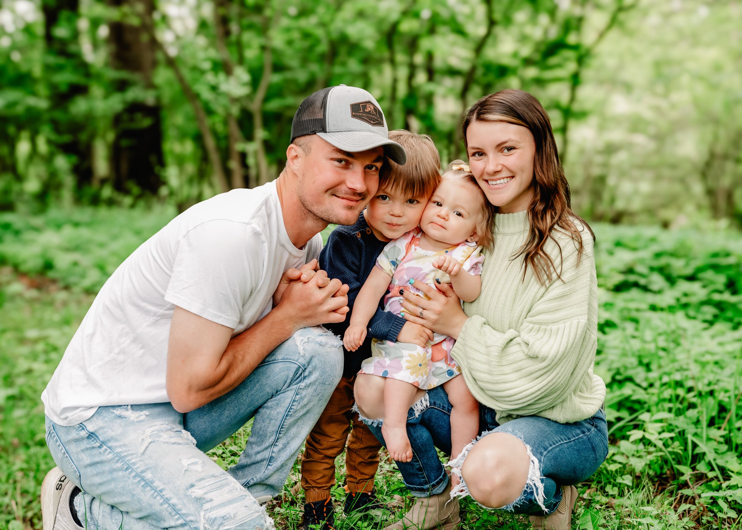 Group of people sitting together outdoors posing for a photo in a lush green forest setting.