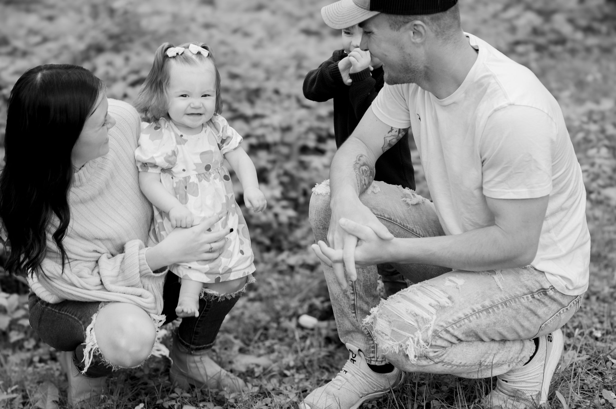 A young family sits together in a natural outdoor setting in black and white photography.
