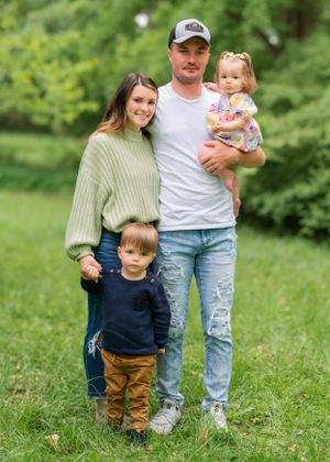 A family poses together on green grass wearing casual clothing on a spring day.