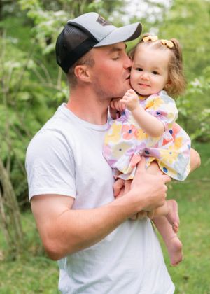 A sweet moment captured outdoors as a toddler in a floral dress receives a gentle kiss in a garden setting.