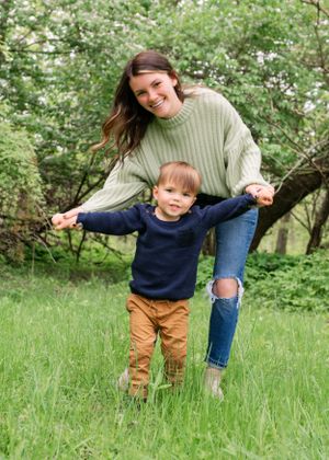 A parent and child play together in a grassy field with blooming trees in the background.