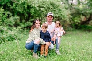 A family sits together on green grass in front of lush foliage during a spring outdoor photo session.