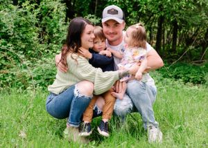 A family sits together outdoors in a grassy area surrounded by green foliage during a spring day.