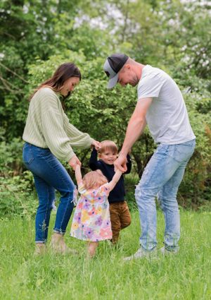 A family plays together in a grassy field on a bright spring day, with greenery and trees in the background.