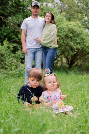 A family poses together in a lush green garden setting with two small children sitting in front of the adults.