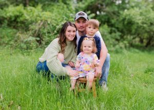 A family of four poses together in a grassy meadow on a sunny afternoon.
