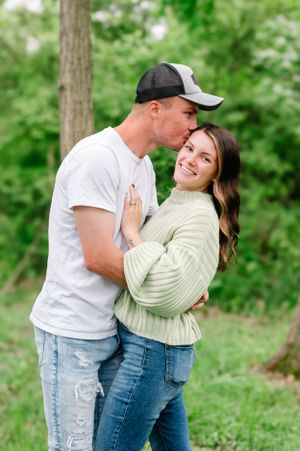A couple share an intimate moment together outdoors in a natural setting with green foliage.