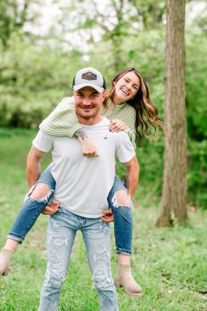 A playful piggyback ride outdoors with green trees and grass in the background.