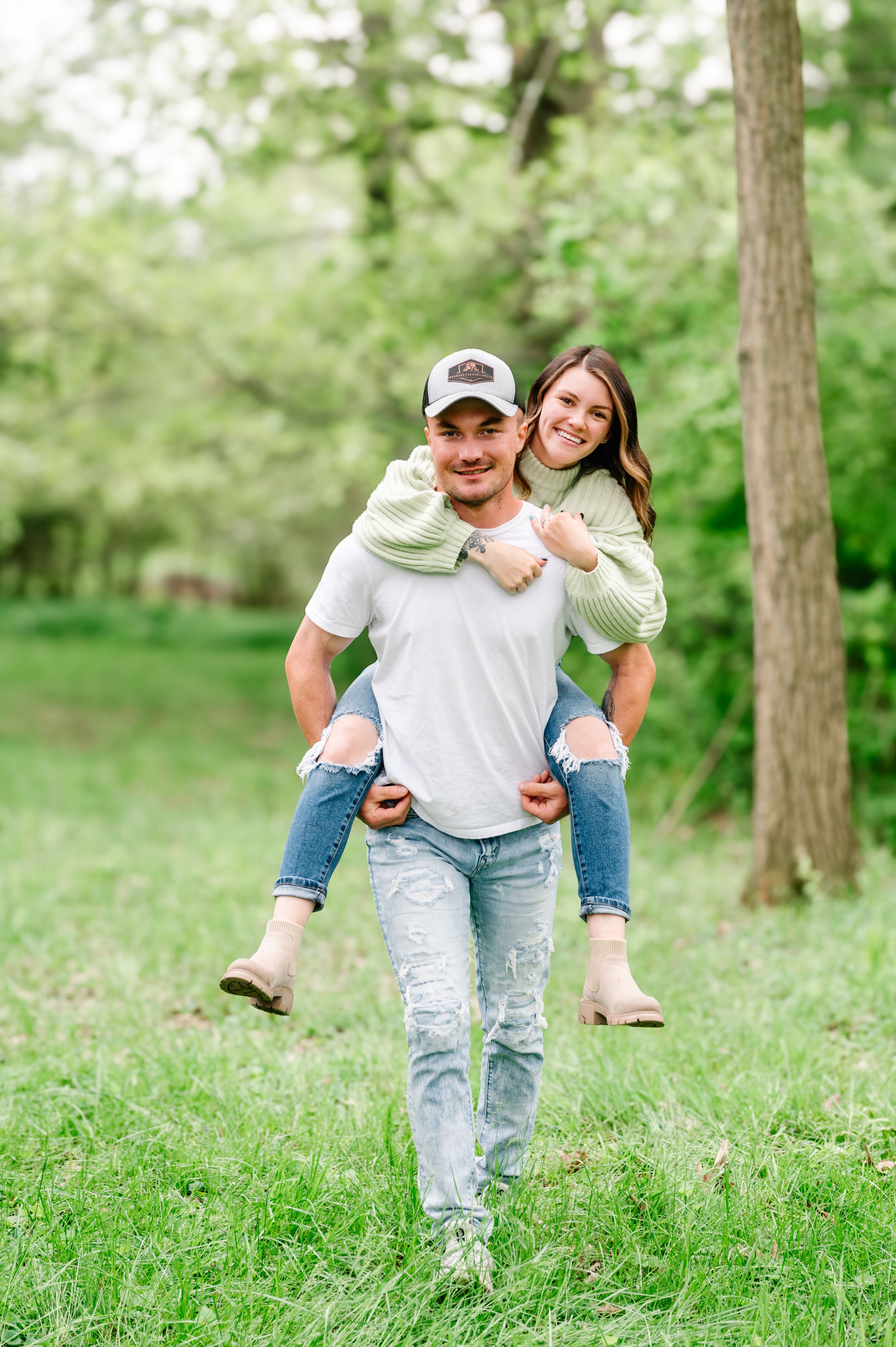 A couple enjoying a playful piggyback ride in a lush green park on a sunny spring day.