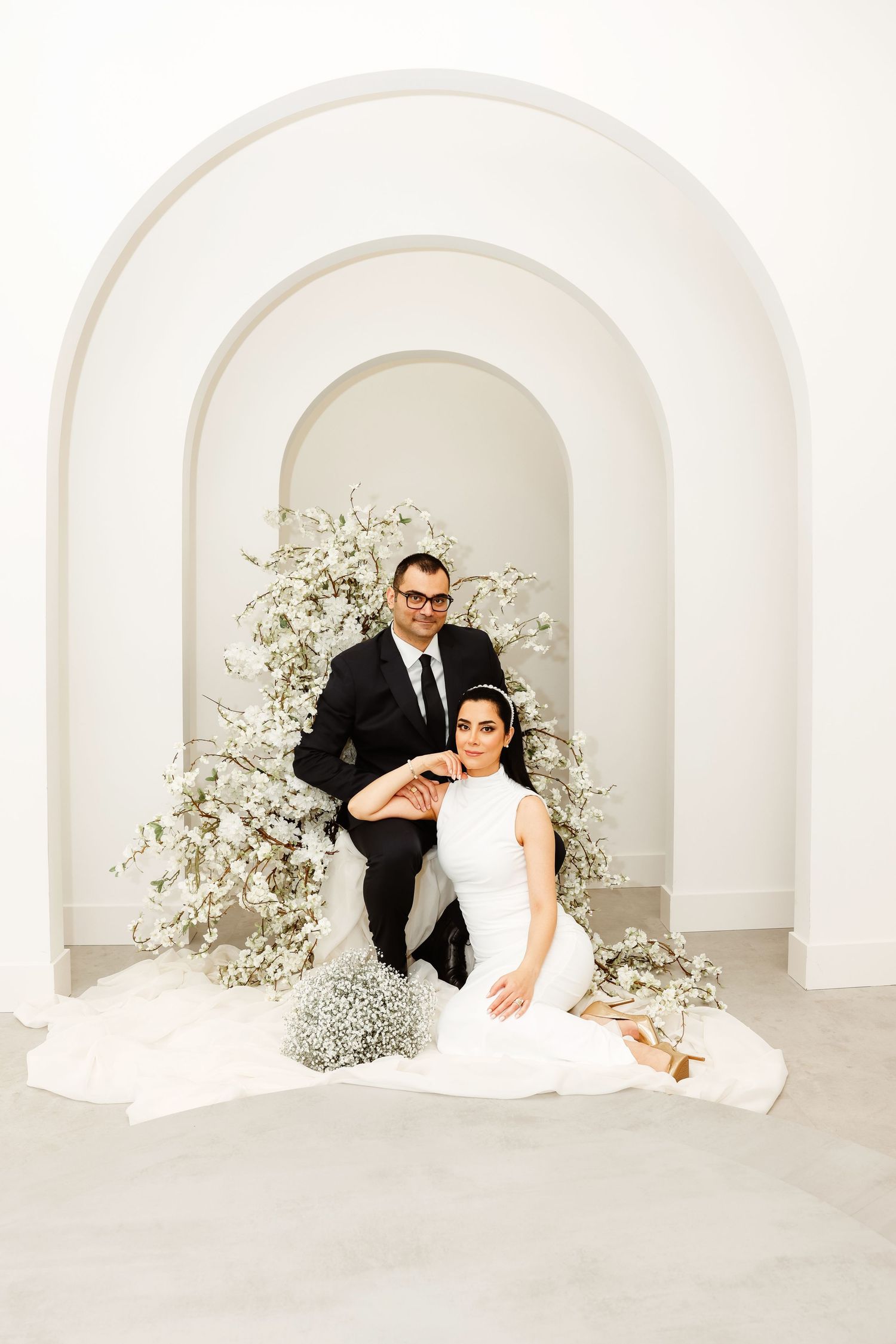 Wedding photo featuring a couple posing in an elegant white archway with baby's breath floral decorations.