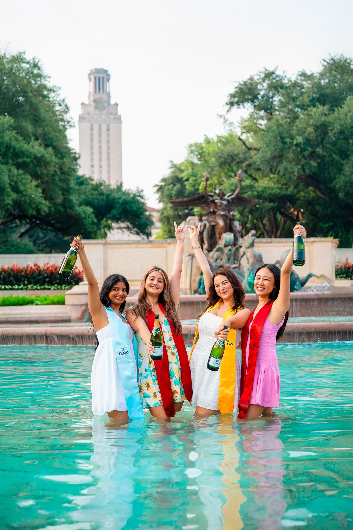 Group celebrating in turquoise pool water with university tower in background.