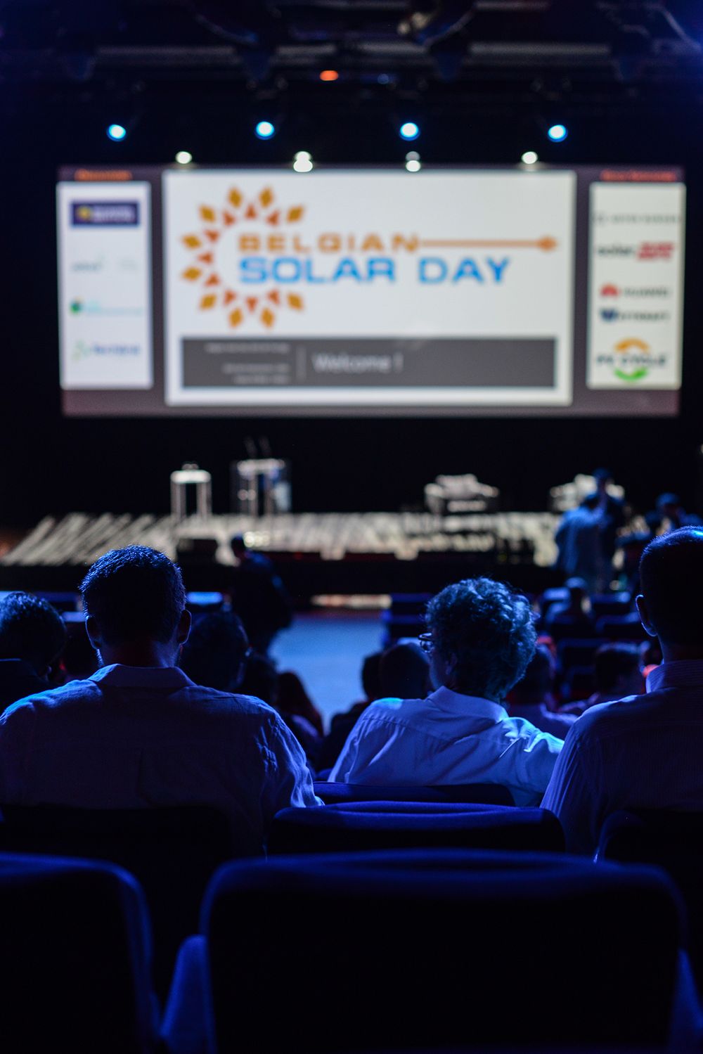 Conference audience in darkened room with projection screen displaying presentation.