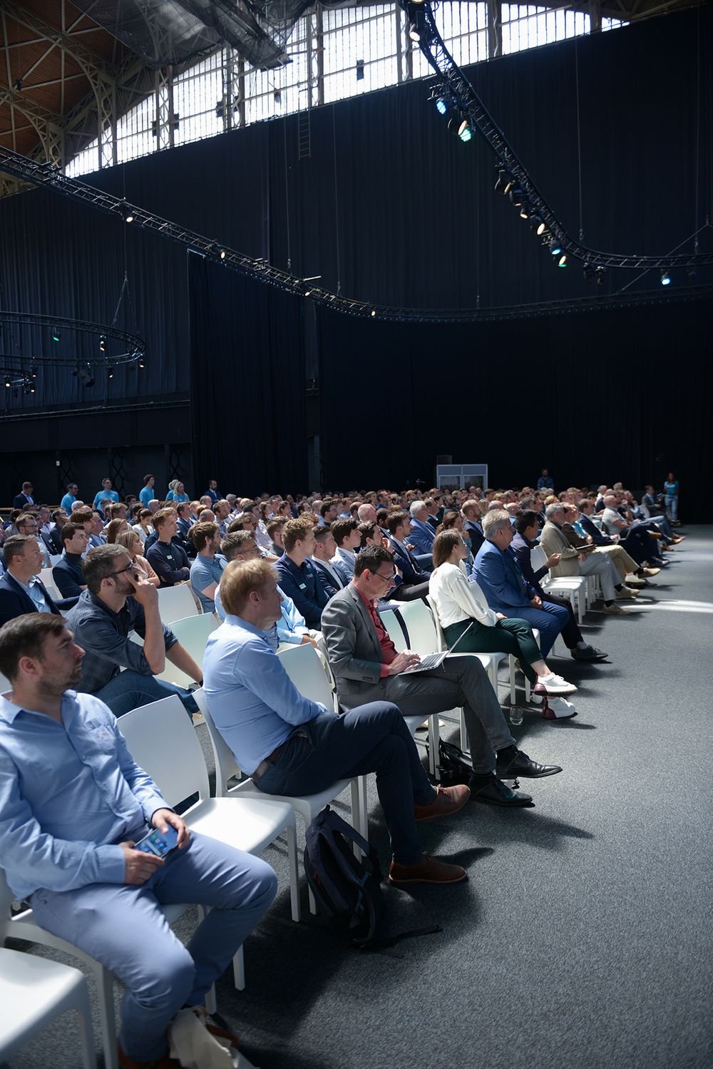 Large conference hall filled with attendees in business attire viewed from elevated angle.