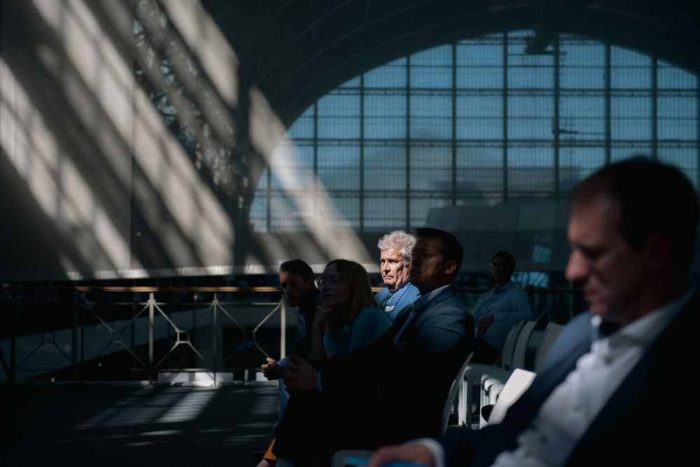 Sunlit conference venue with arched windows and attendees in seats.