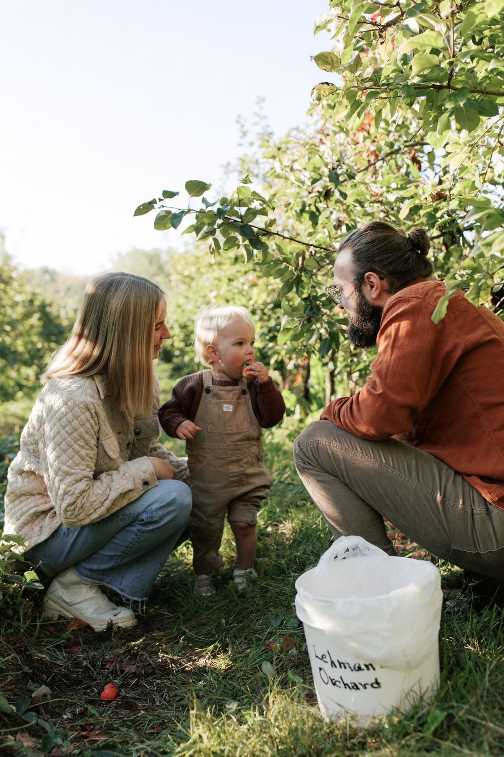 A family picks apples together in an orchard with a white bucket nearby.