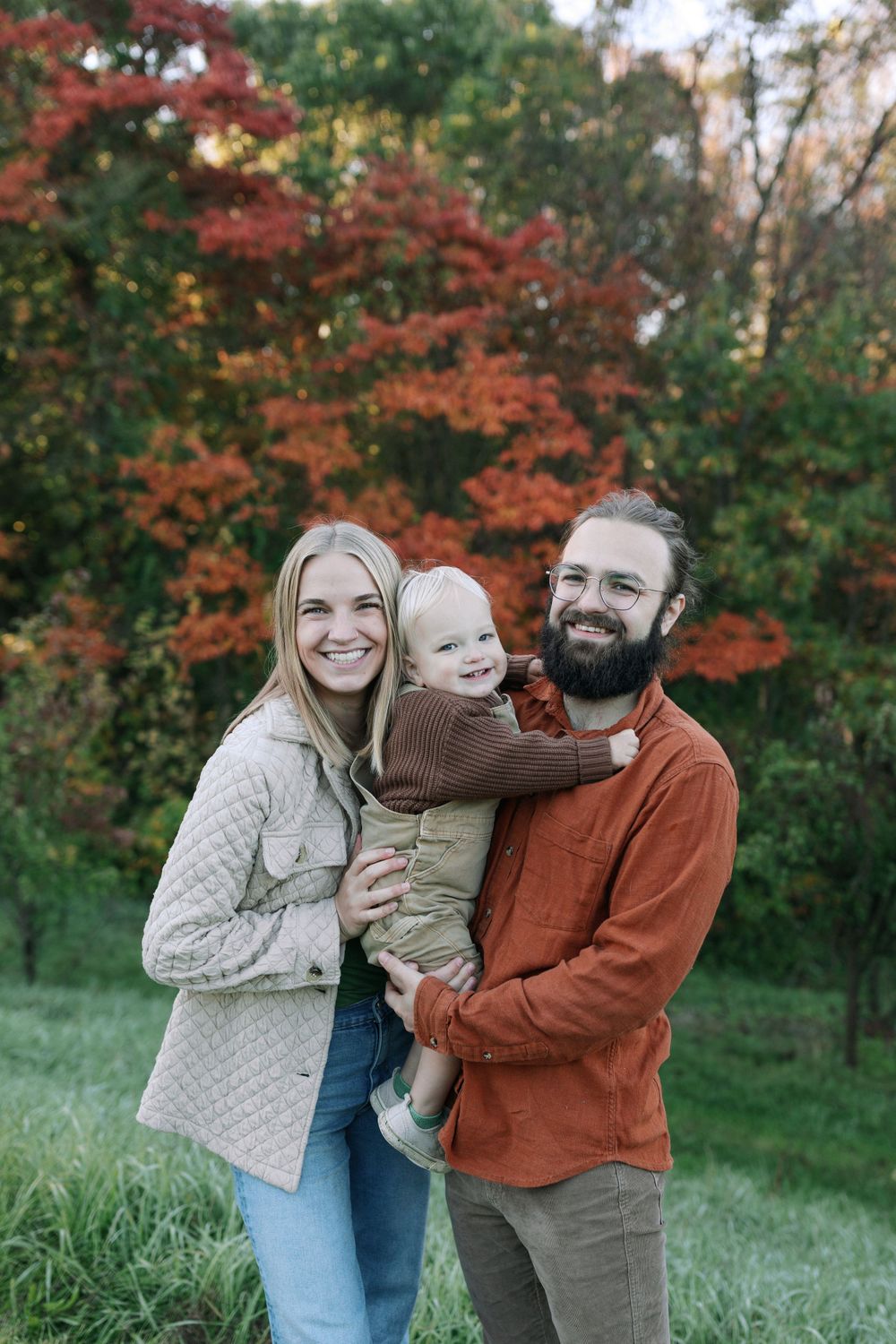 A joyful family portrait with vibrant red autumn foliage in the background.