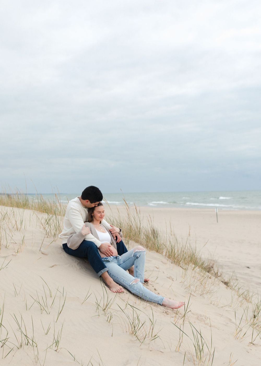 A romantic moment shared between two people sitting on coastal sand dunes.