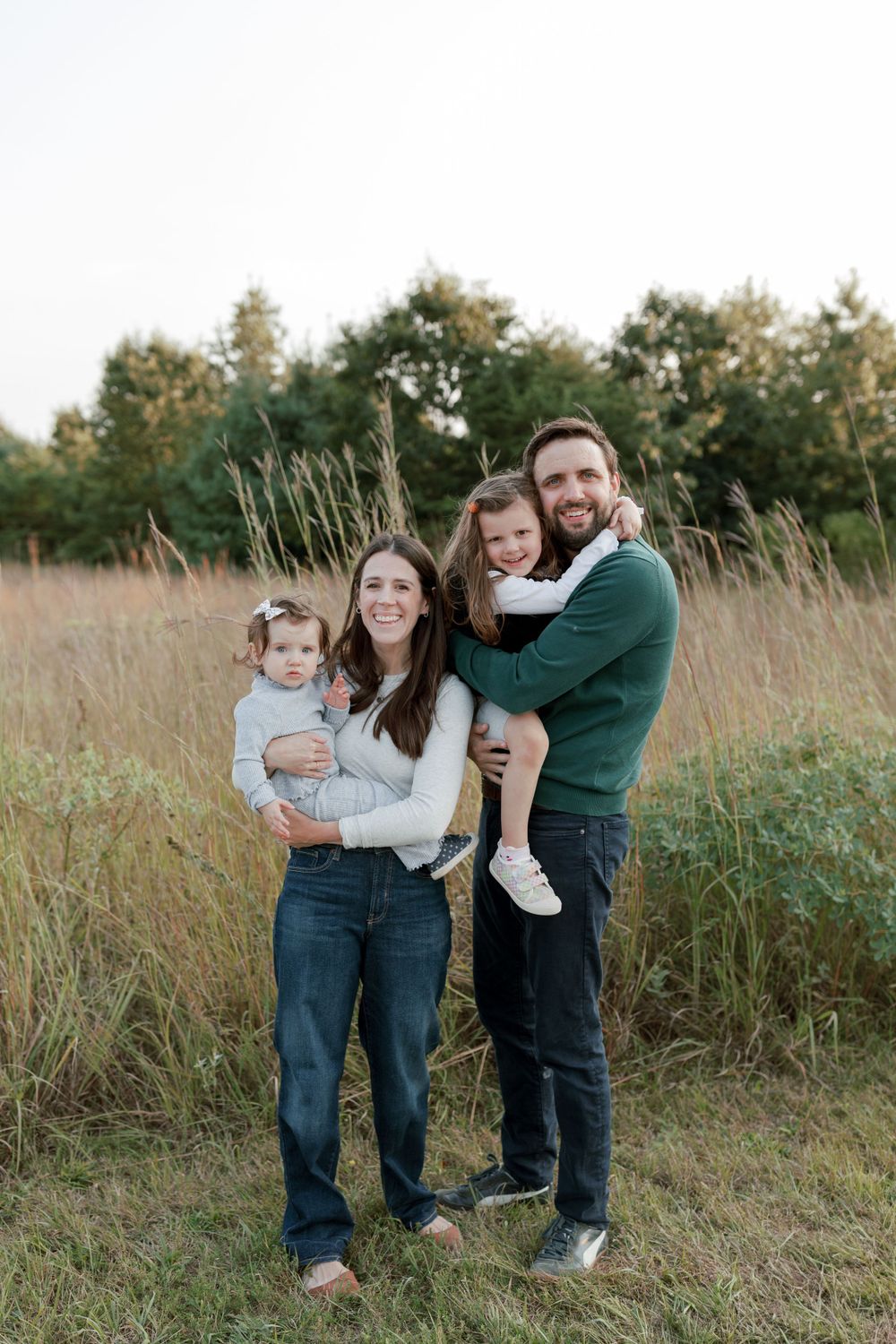 A family of four poses together in a golden field at sunset.