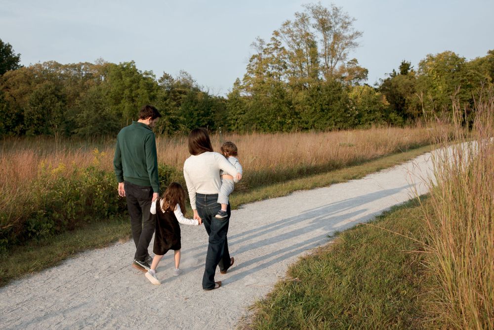 A family walks together on a winding path through autumn fields.