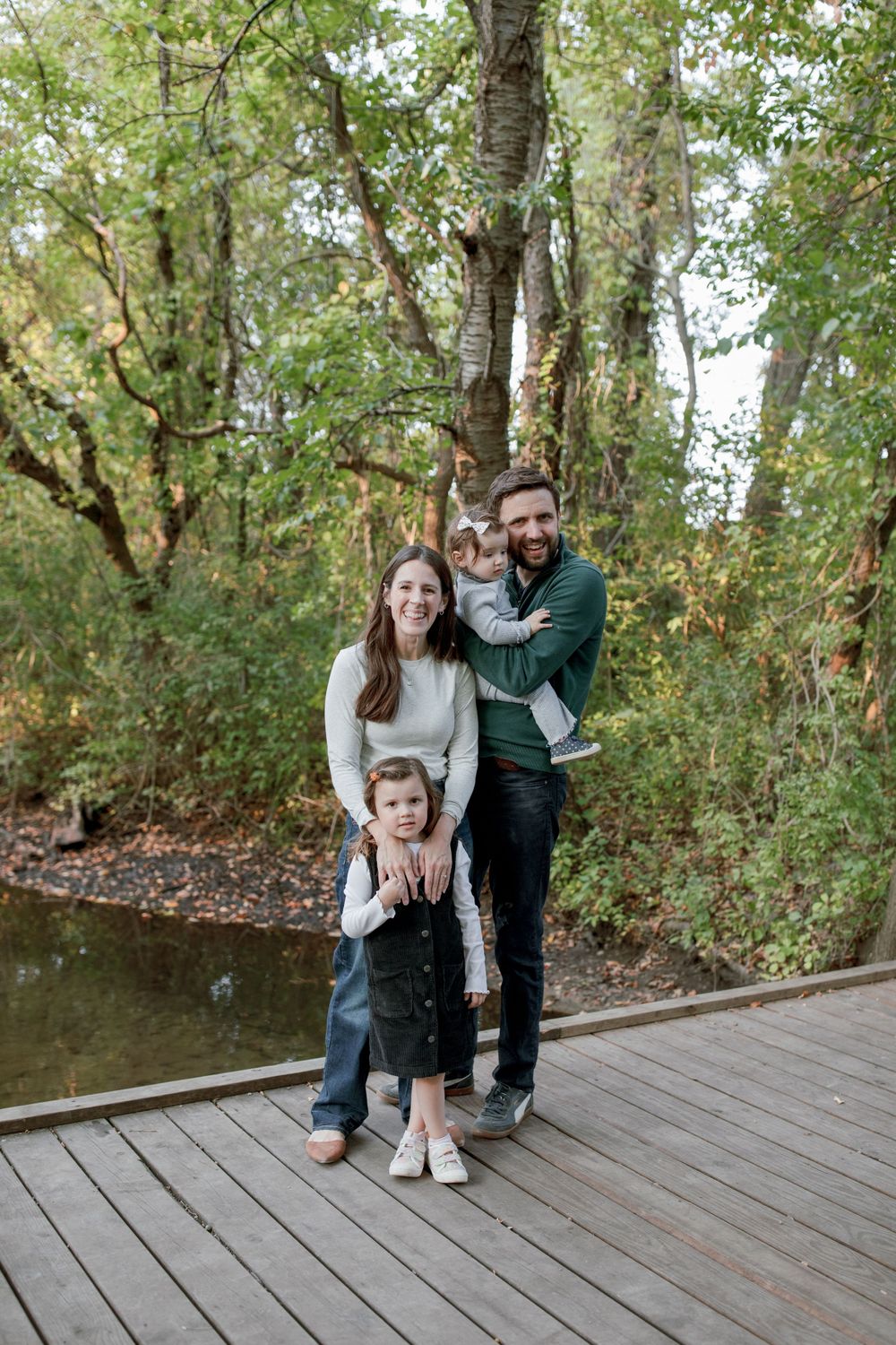 A family poses together on a wooden deck overlooking a stream in a wooded setting.