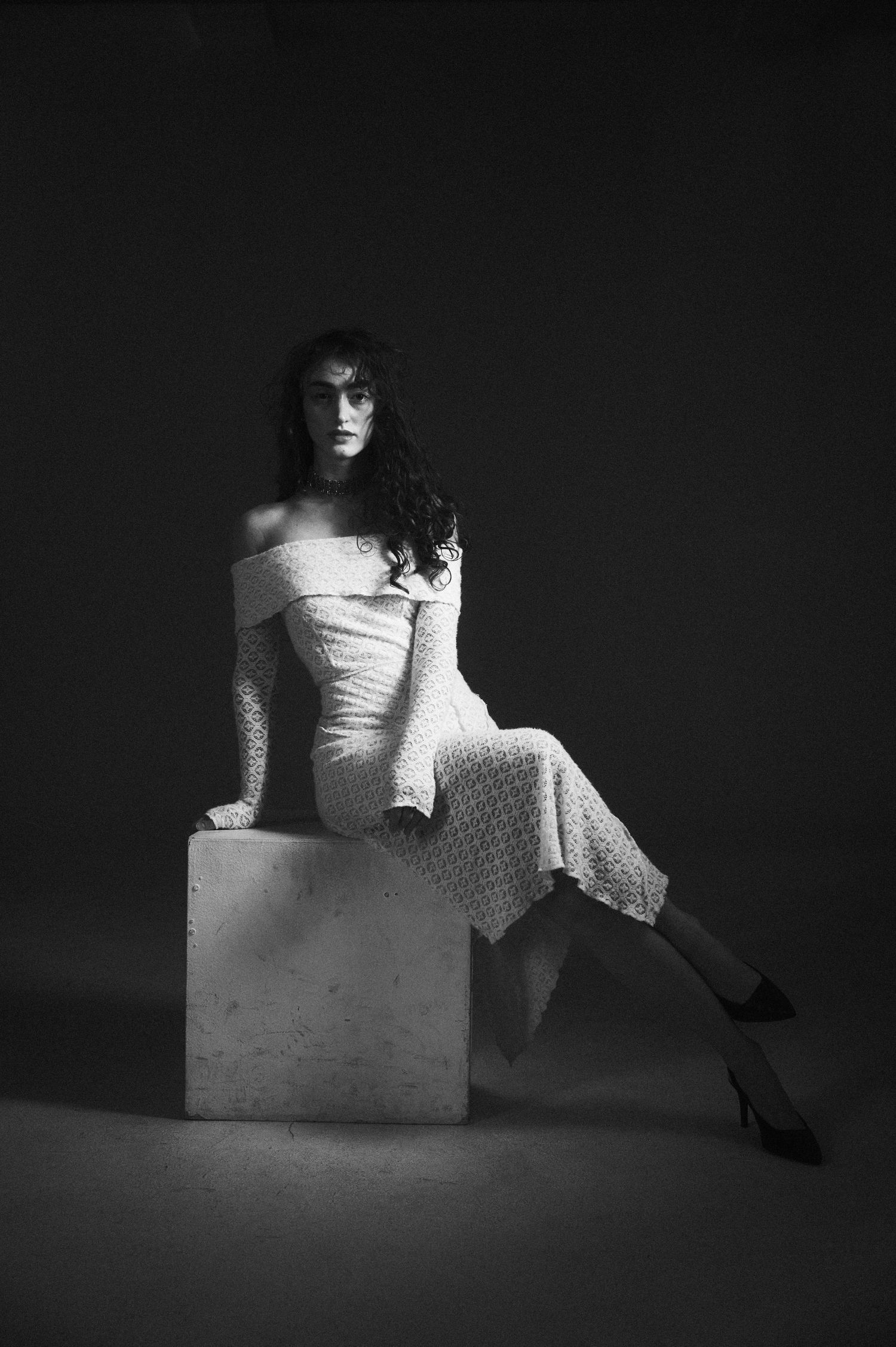 Artistic black and white portrait of someone seated on a cube in a white dress.