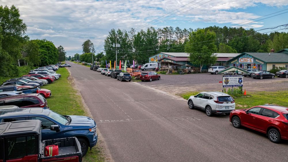 Aerial view of a busy rural roadside attraction with full parking lot and small shops surrounded by trees.
