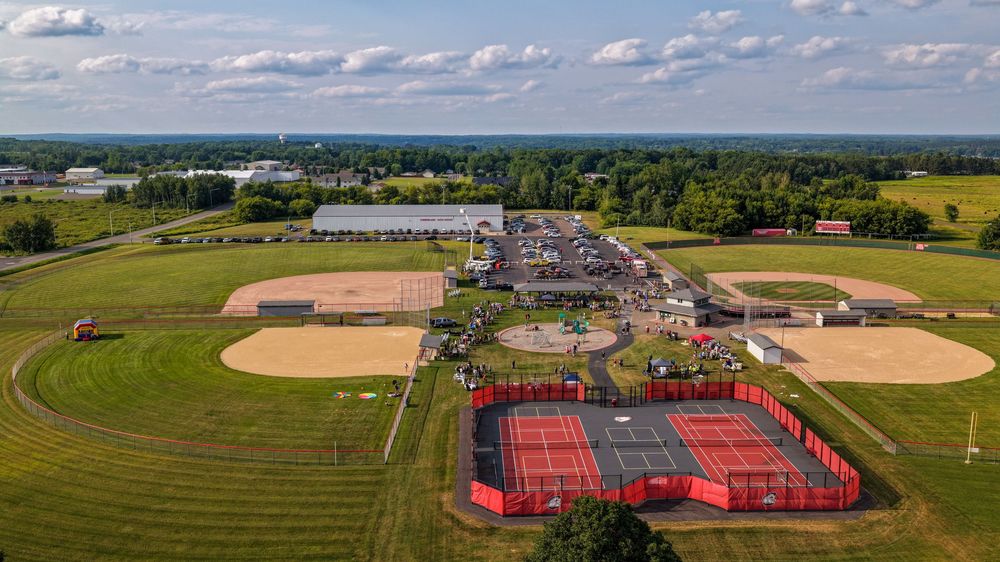 Aerial view of a sports complex with baseball fields and red tennis courts surrounded by green landscape.