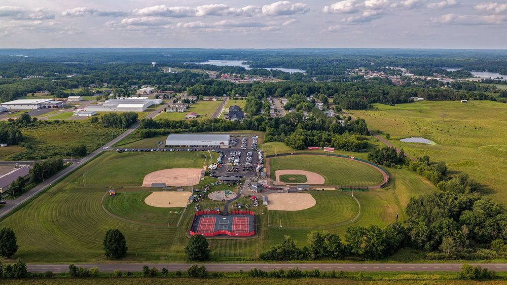 Aerial view of a sports complex with baseball fields, tennis courts, and green landscapes in a suburban town.