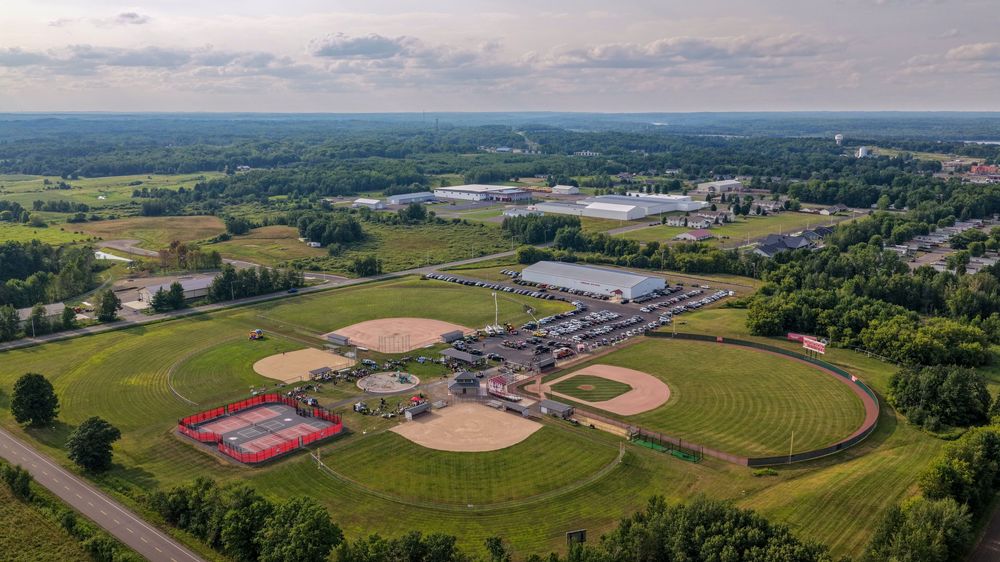 Aerial view of a sports complex with baseball fields, tennis courts, and green landscapes in a suburban setting.