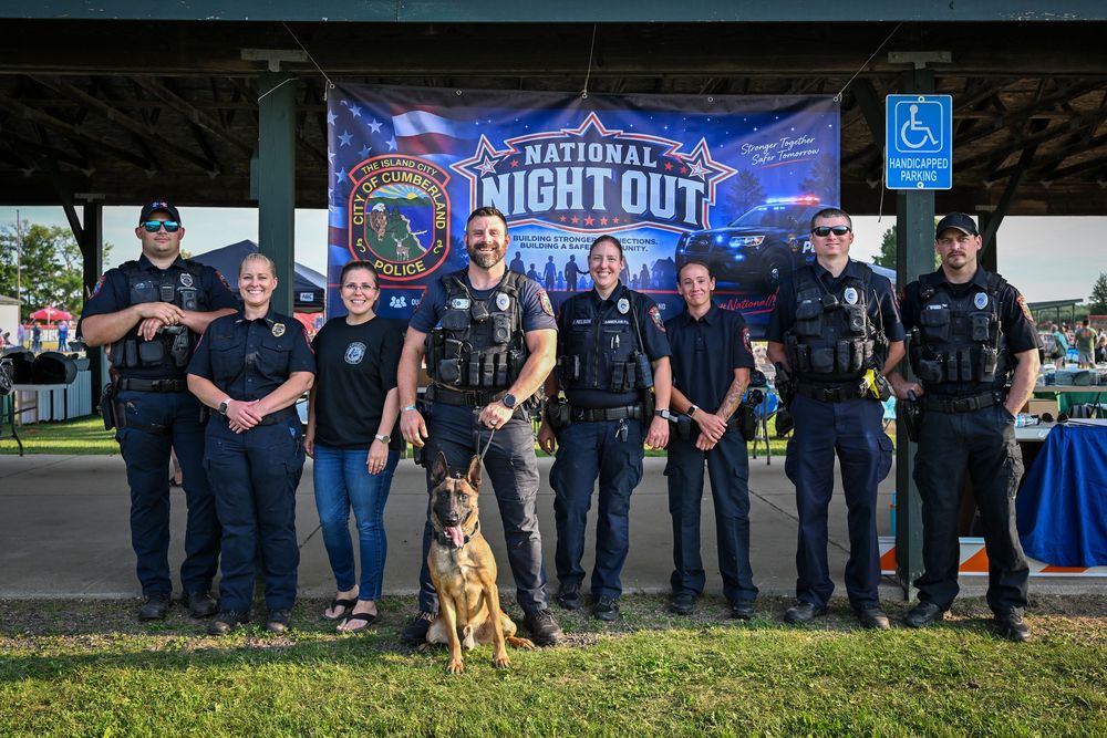 Group of police officers and K9 unit posing at National Night Out community event under a banner outdoors.