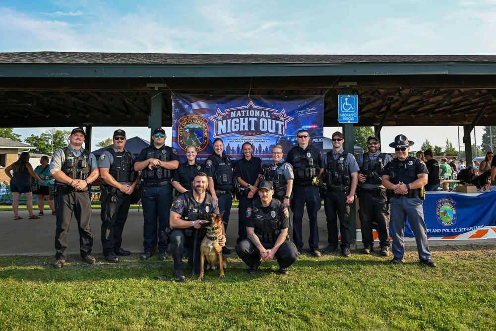 Law enforcement officers pose together at National Night Out community event with a K9 dog under a pavilion.