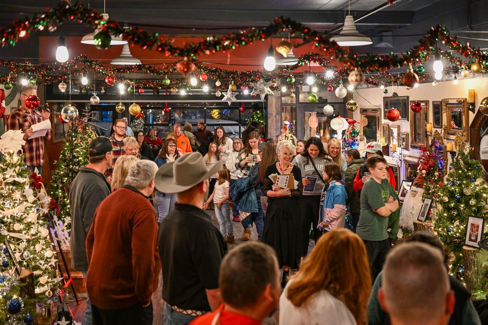 Festive indoor Christmas market with crowds of people browsing decorated trees and holiday displays under string lights.