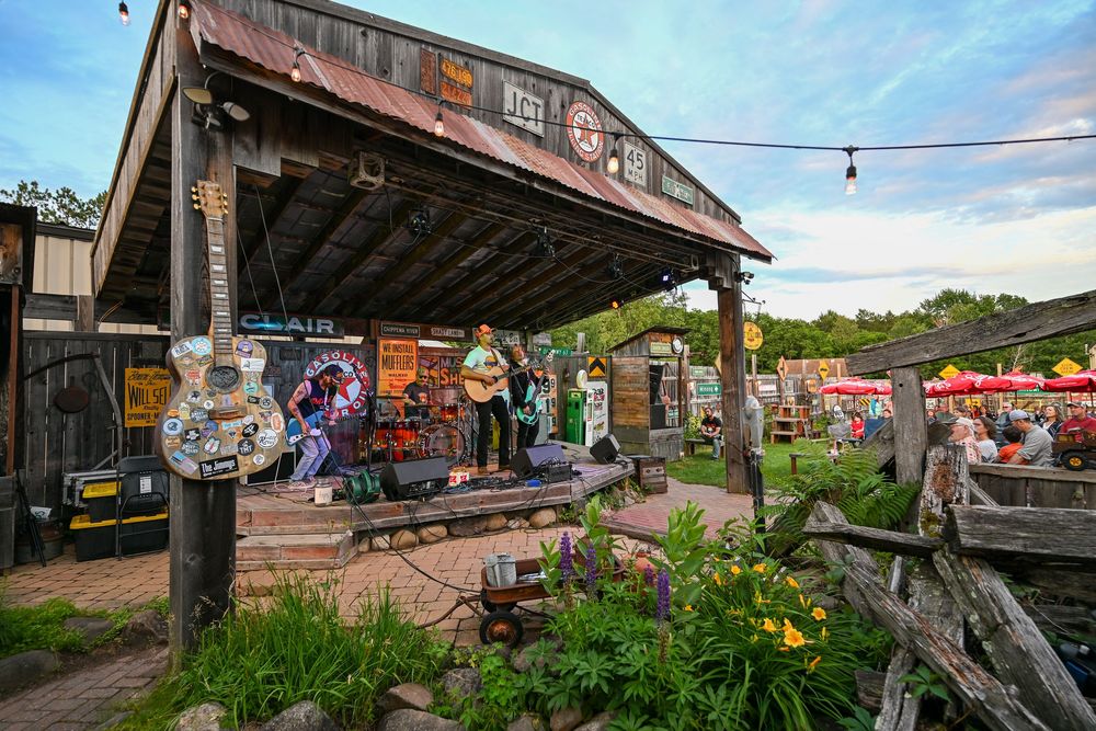 Live band performing on a rustic outdoor stage at a charming country music venue at dusk.