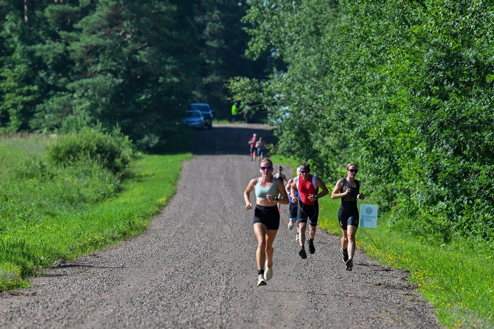 Runners racing down a sunny gravel path surrounded by lush green trees and grass.