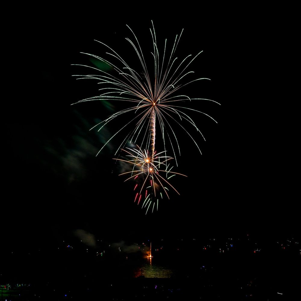 Colorful fireworks burst against a dark night sky above a small town.