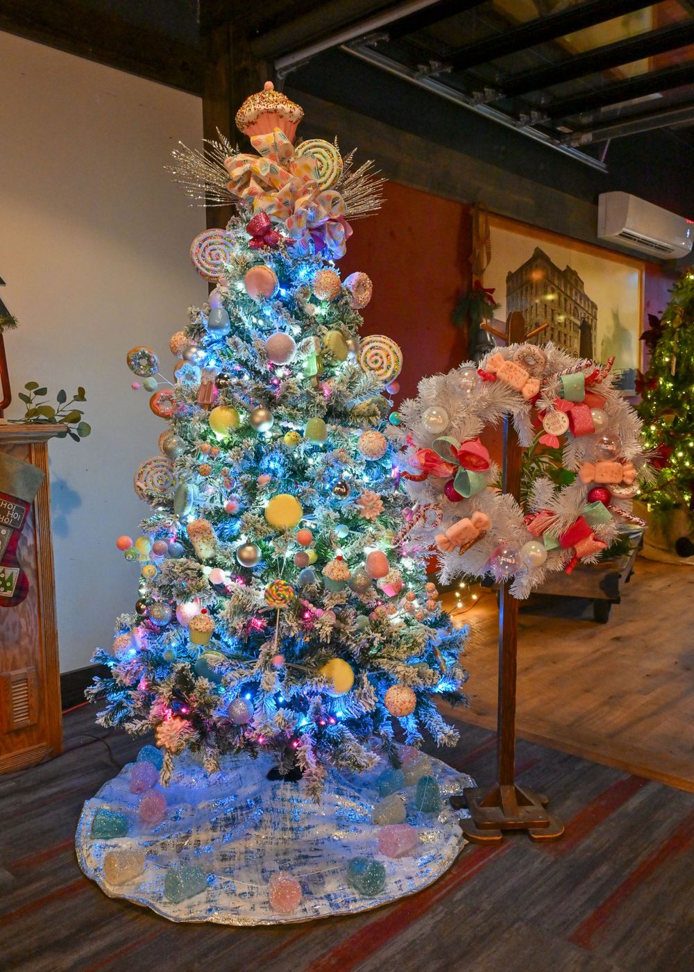 Colorful candy-themed Christmas tree with blue lights, lollipop ornaments, and angel topper beside matching wreath.