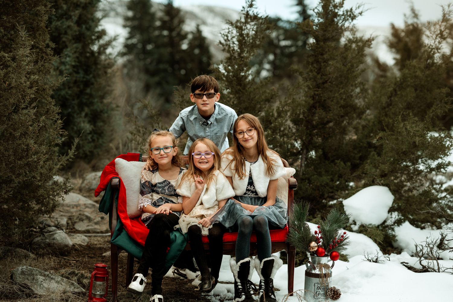 A family gathering on snowy ground surrounded by pine trees during a winter photoshoot.