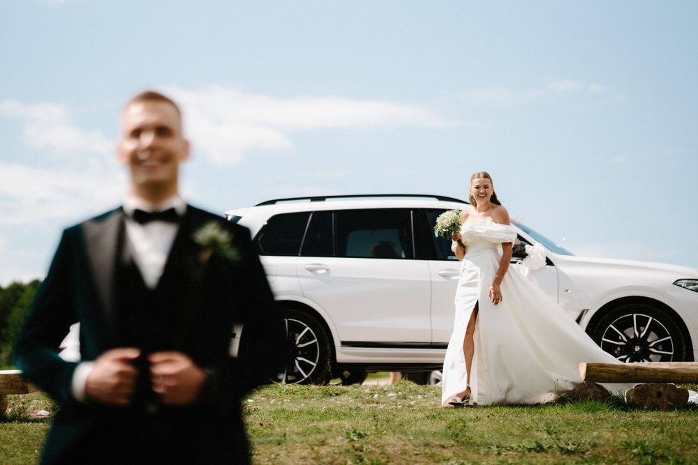 Wedding party poses near white vehicles on a sunny day by the water.