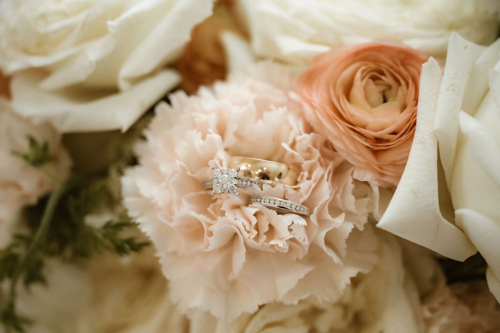Close-up of blush pink roses and white flowers with a sparkling diamond ring nestled among the petals.