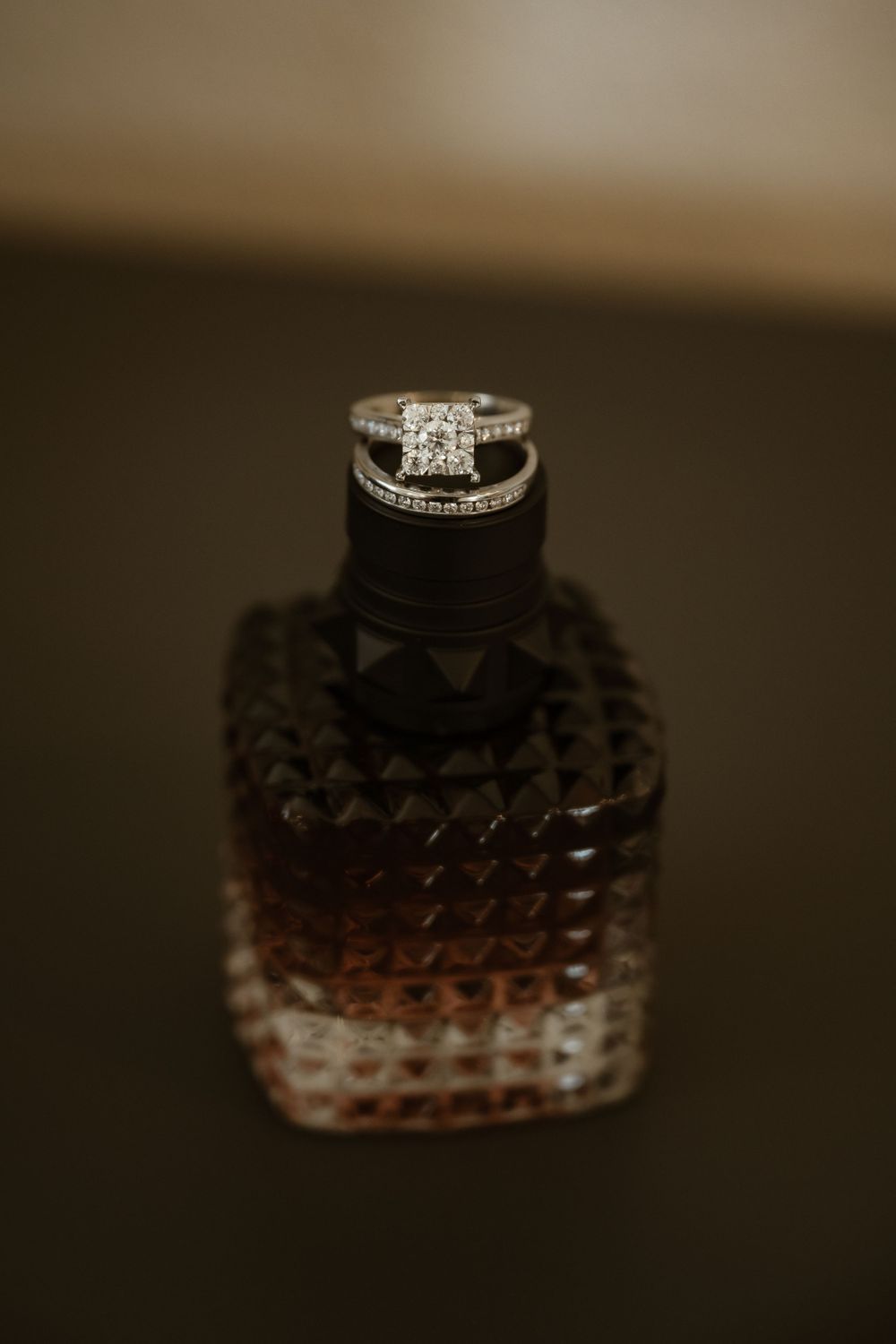 Diamond engagement ring displayed on a textured dark glass surface with artistic lighting.