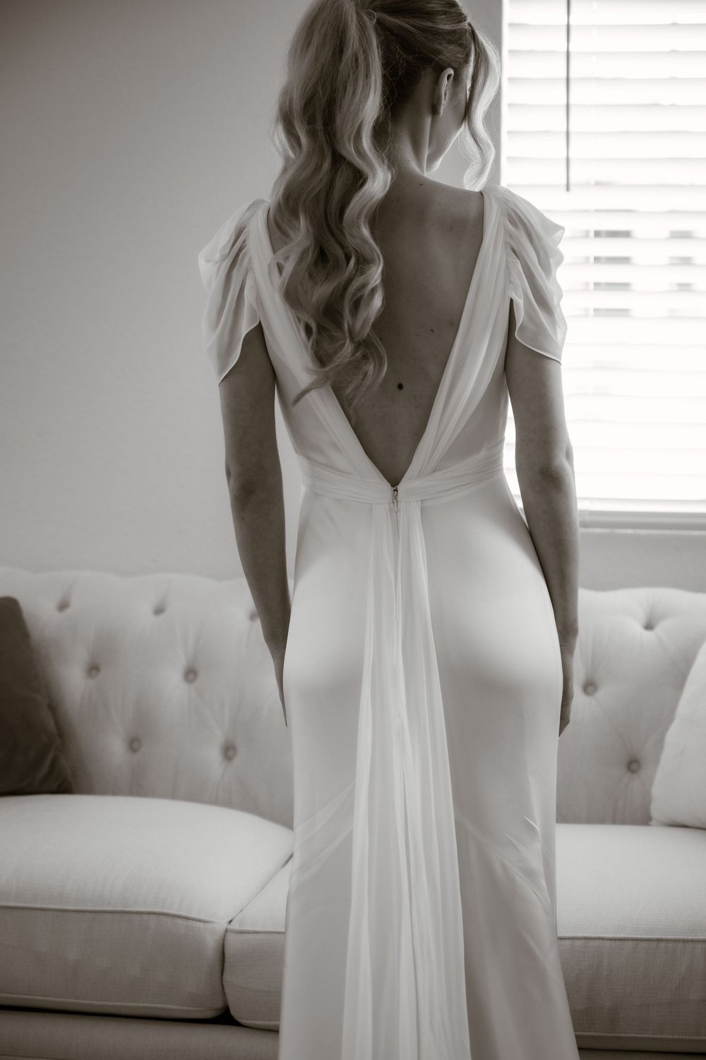 Back view of a flowing white wedding gown with delicate cap sleeves against a light background.