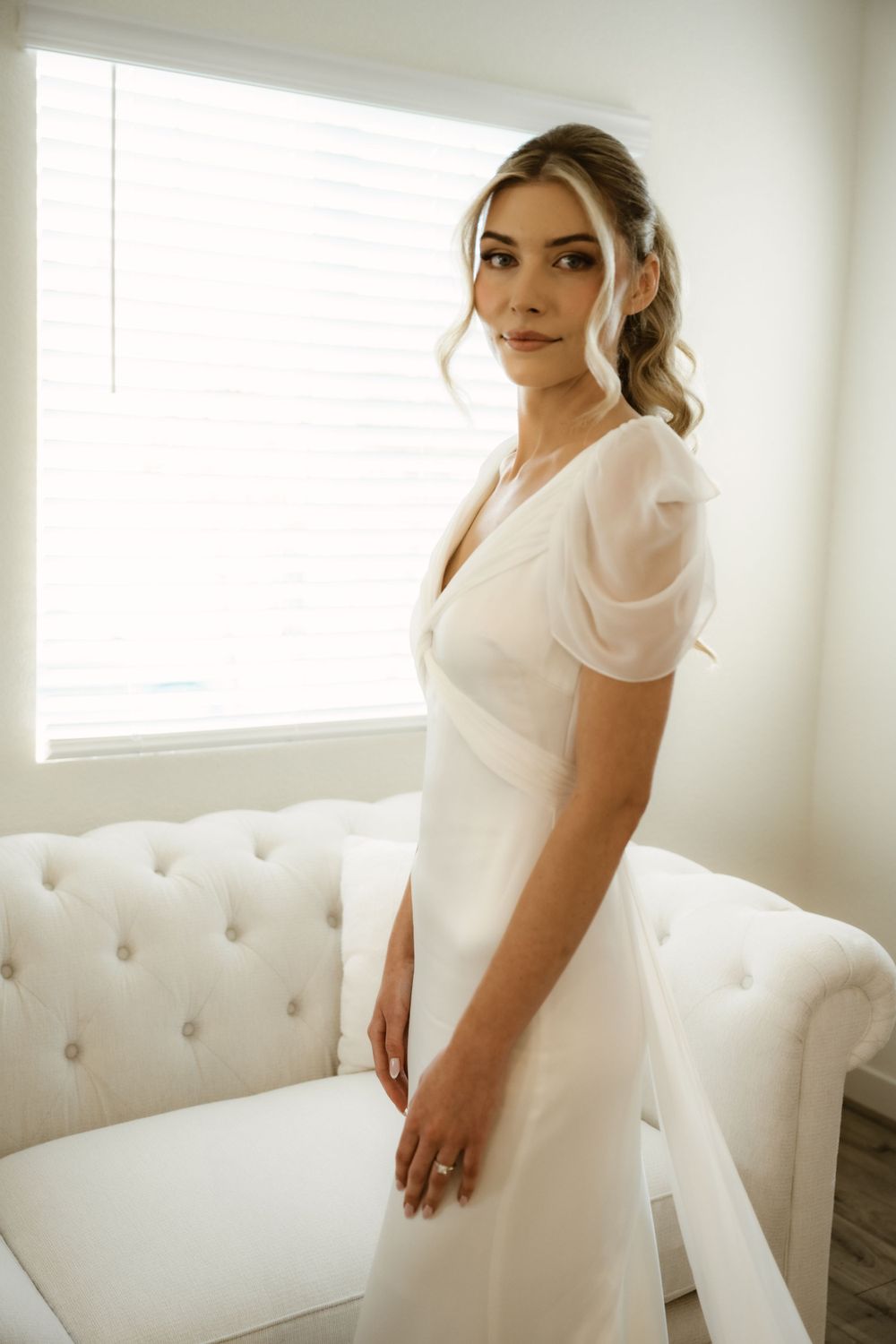 Classic white wedding dress with v-neckline photographed against a bright interior setting.